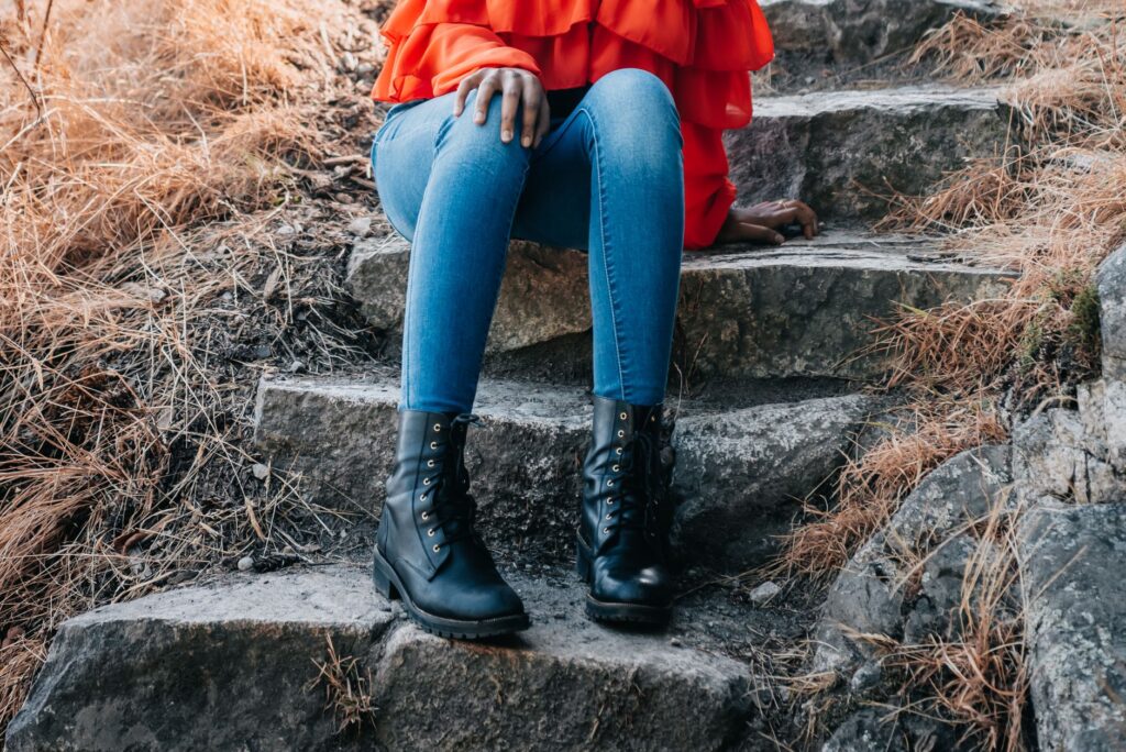 Woman in stylish boots and jeans sitting on outdoor stone steps in autumn setting.