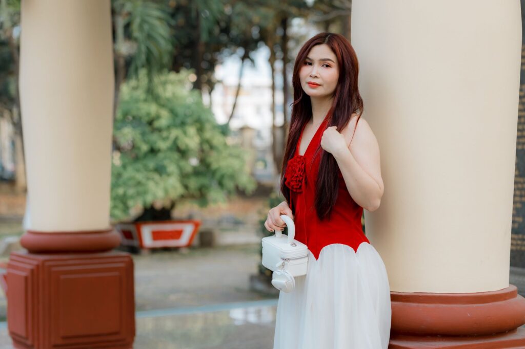 Woman in a stylish red and white dress posing outdoors against a column.
