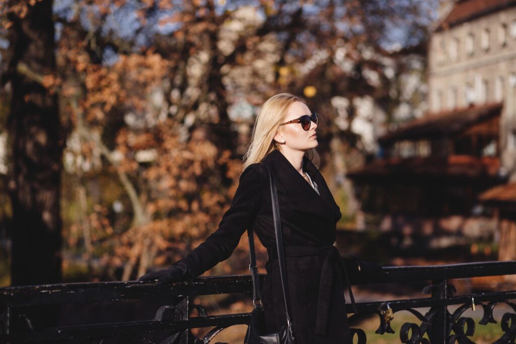 Fashionable woman in black coat and sunglasses standing on a city bridge during fall.