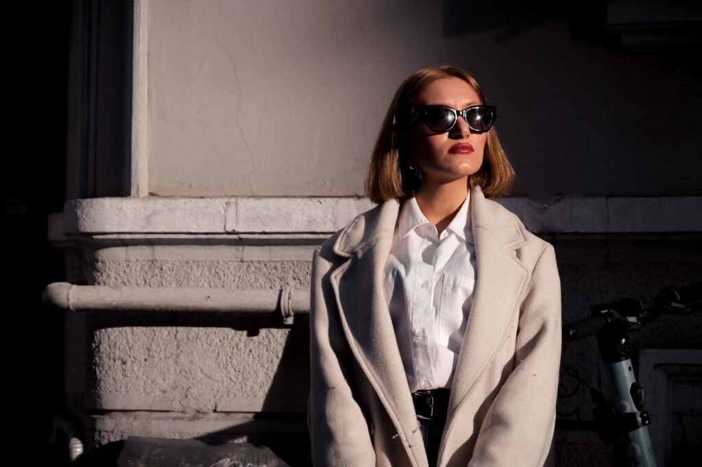 Fashionable woman wearing sunglasses posing against a city wall wearing a stylish coat.