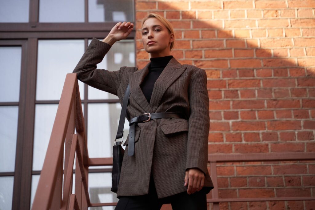 Confident woman posing on a staircase in a stylish blazer against a brick wall. Ideal for fashion and lifestyle themes.