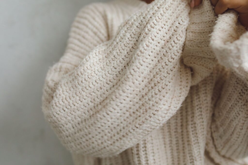A woman wearing a cream fine-knit sweater with simple gold jewelry and neutral pants