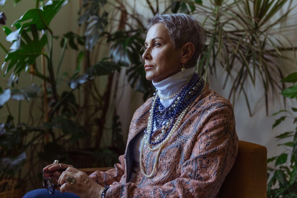 An elegant senior woman in boho style sitting amidst indoor plants, deep in thought.