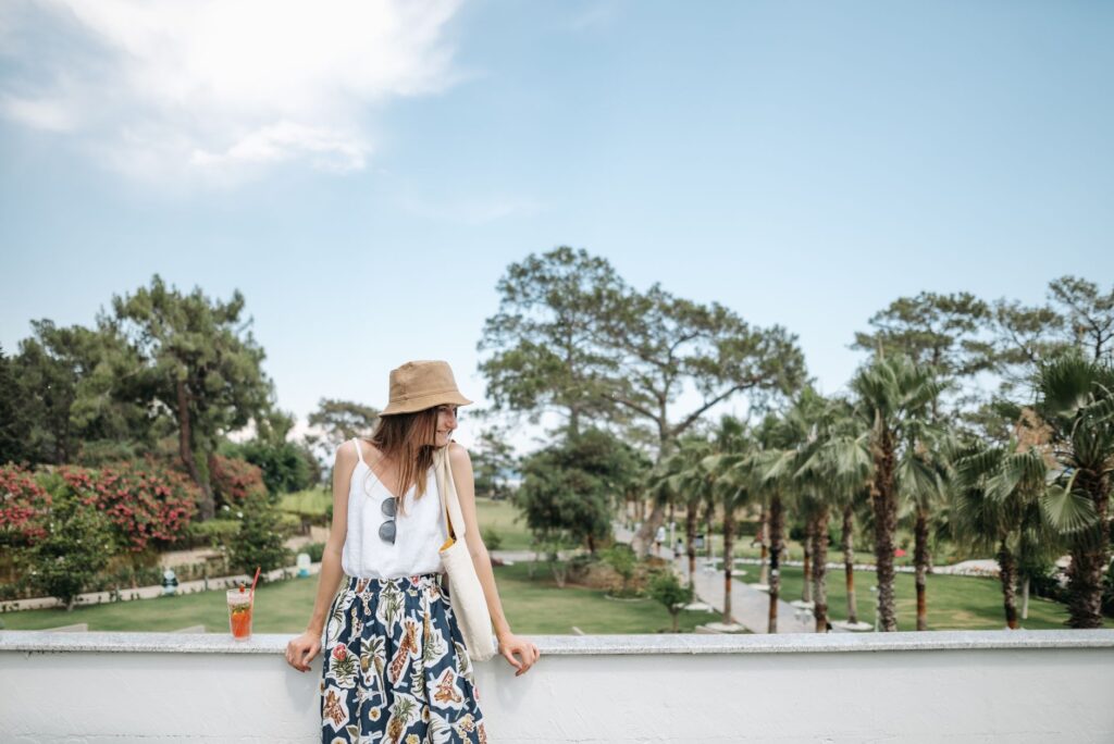 A woman enjoys the view from a balcony in a lush tropical resort with palm trees and blue skies.