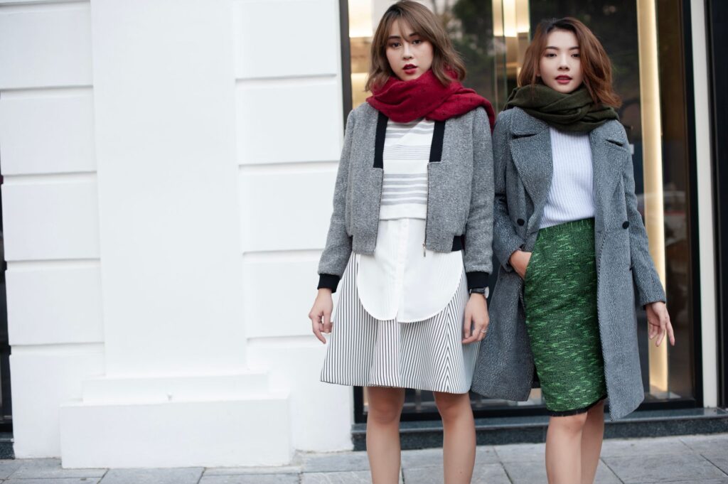Two women wearing stylish winter coats and scarves posing confidently outdoors.