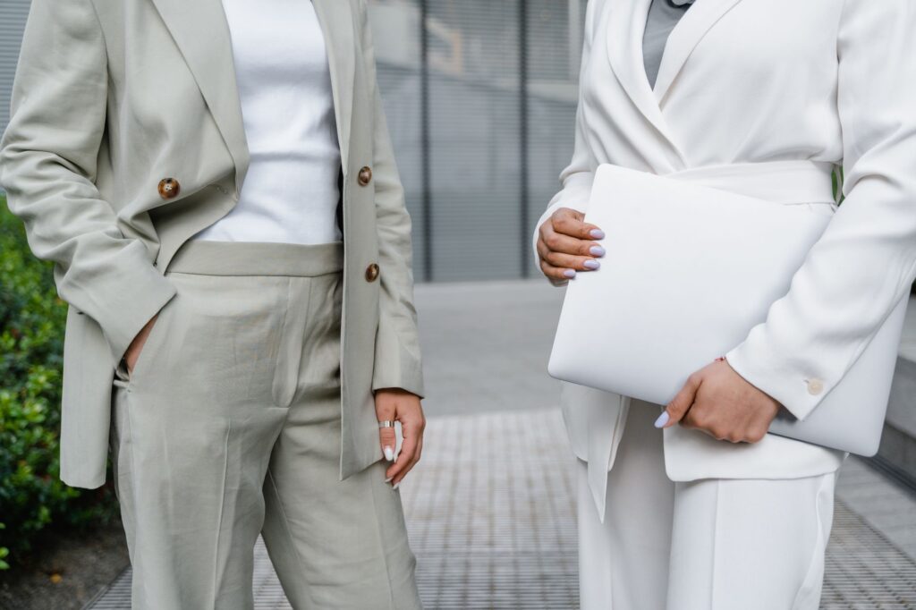 Two business professionals in modern blazers holding a laptop outdoors.