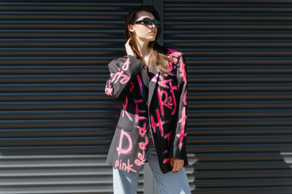 Stylish woman wearing sunglasses and graffiti blazer posing outdoors. Trendy street style fashion.
