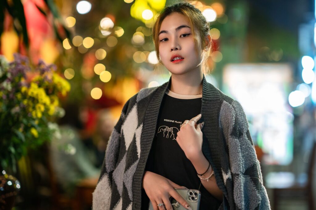Portrait of a young woman with a smartphone in a vibrant urban night scene, exuding style and confidence.