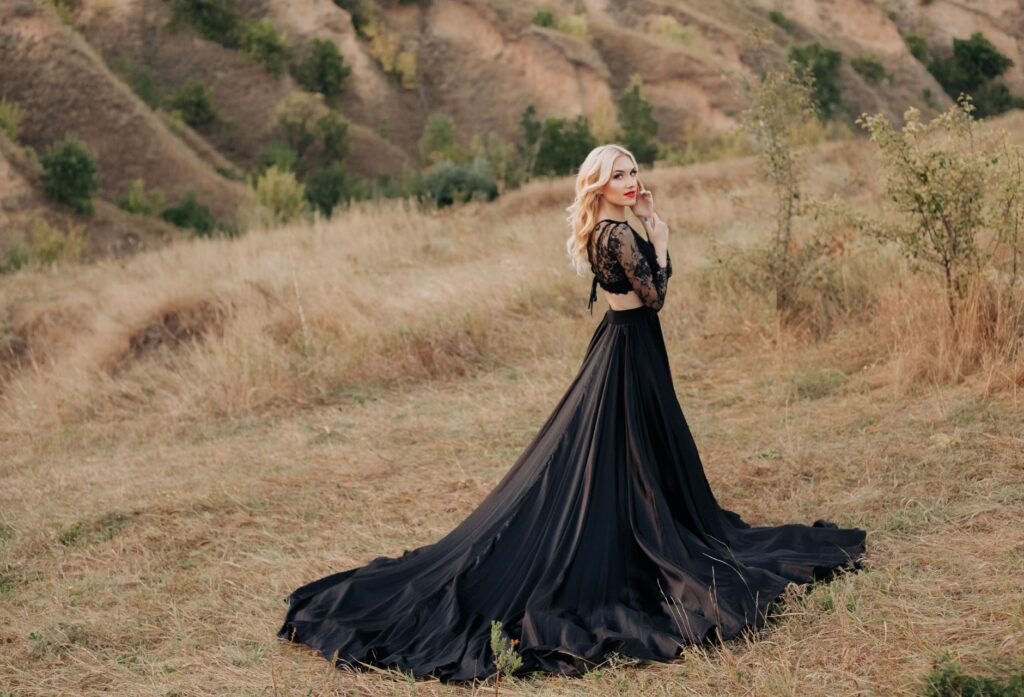 Blonde woman in a black maxi dress poses gracefully in a rural meadow in Dnipro, Ukraine.