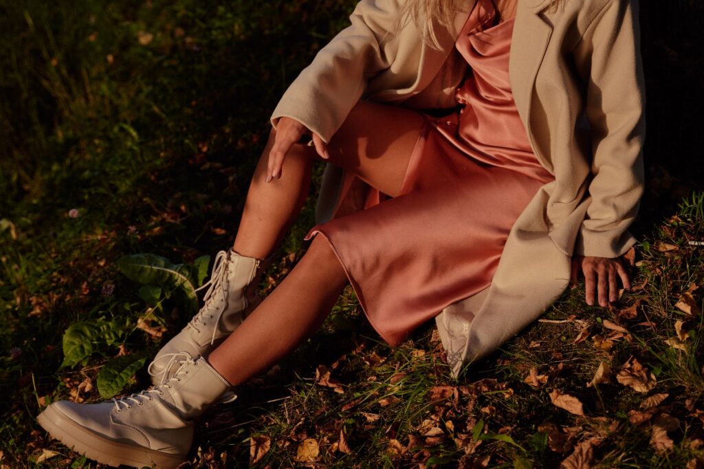 An elegantly dressed woman in a coat sits among fall leaves in evening light, exuding warmth.