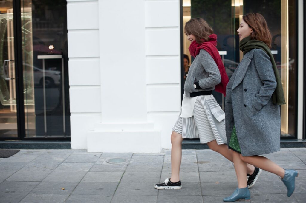 Two women walking stylishly in urban setting wearing elegant coats and scarves.