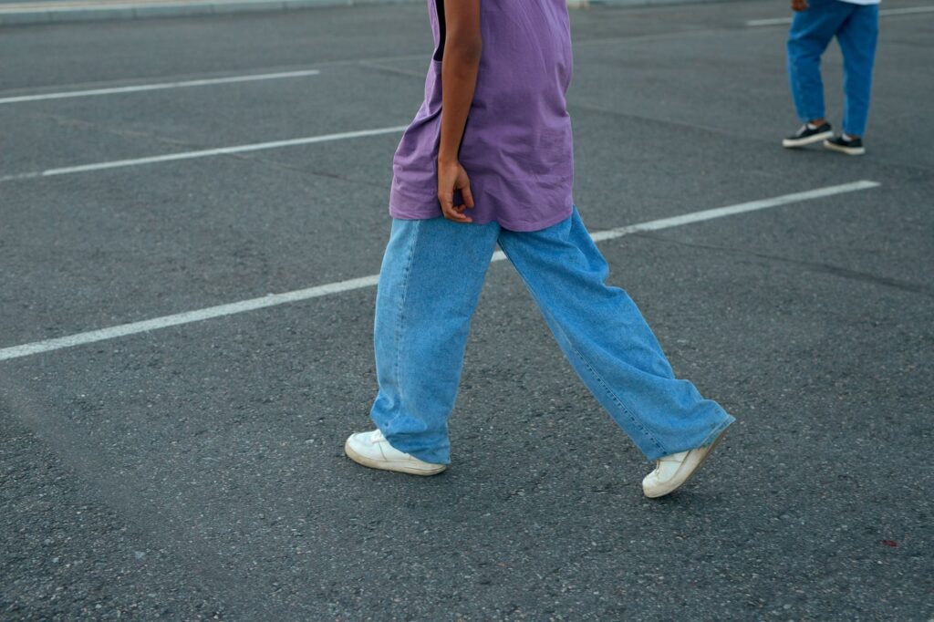 Unrecognizable person walking in a parking lot wearing a purple top and denim jeans.