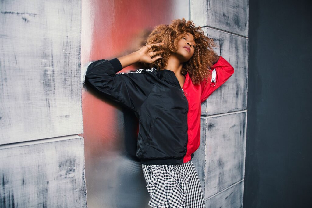 Fashionable woman posing with curly hair against a textured urban wall.
