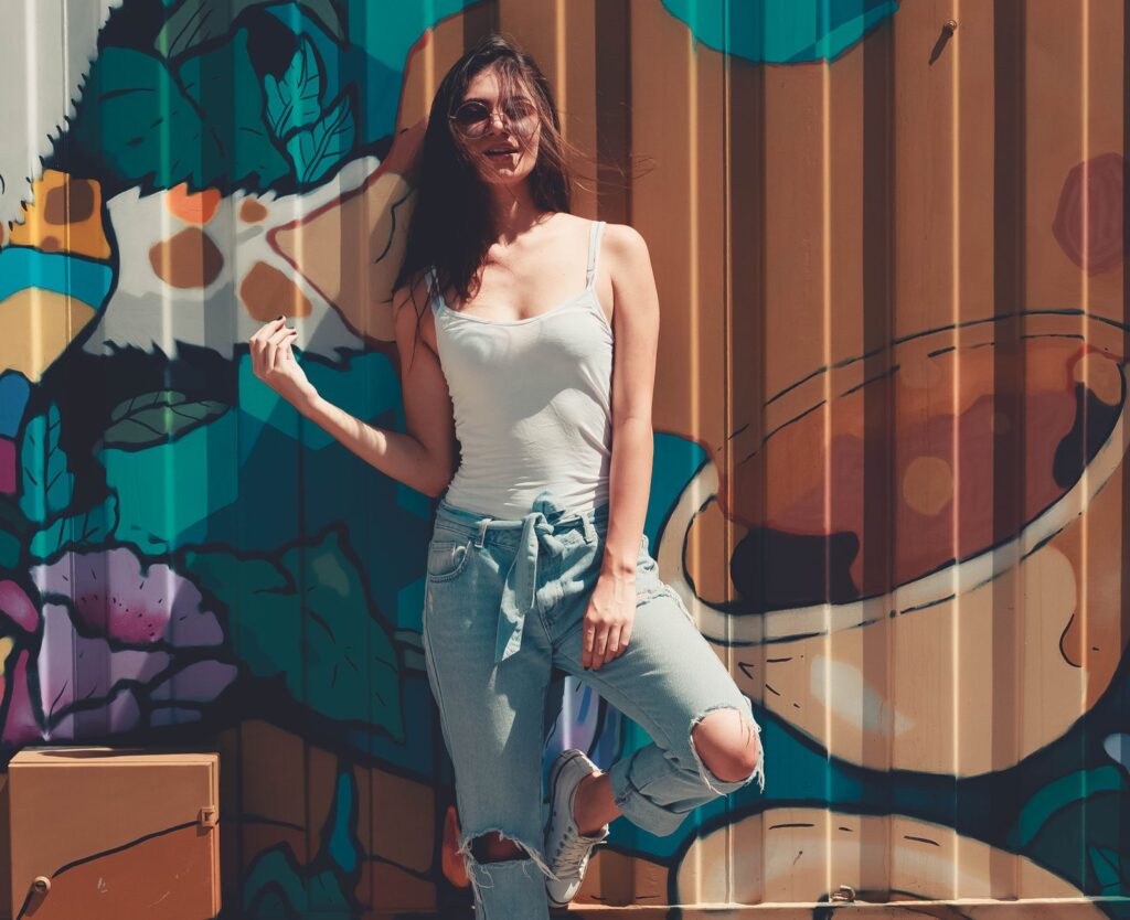 Fashionable woman in casual outfit posing by a vibrant graffiti wall in daylight.
