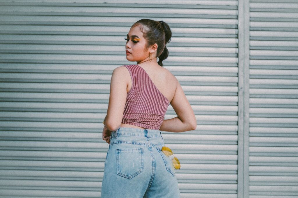 Fashionable woman in denim and one-shoulder top posing outdoors by a roll-up door.