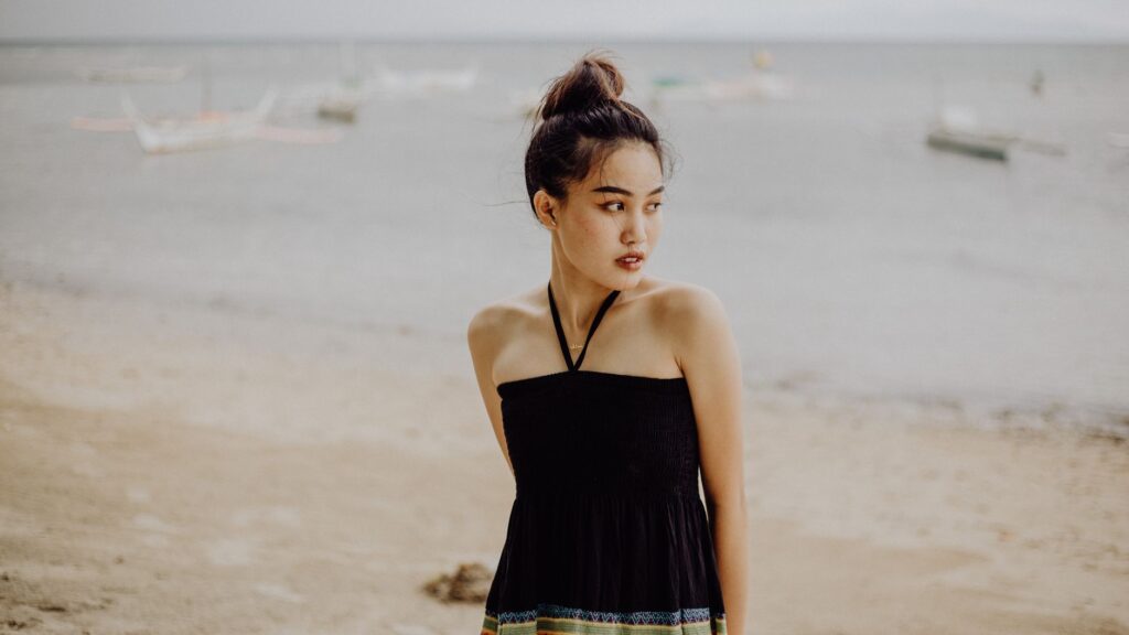 Elegant woman in a halter top on a serene Philippine beach with boats in the background.