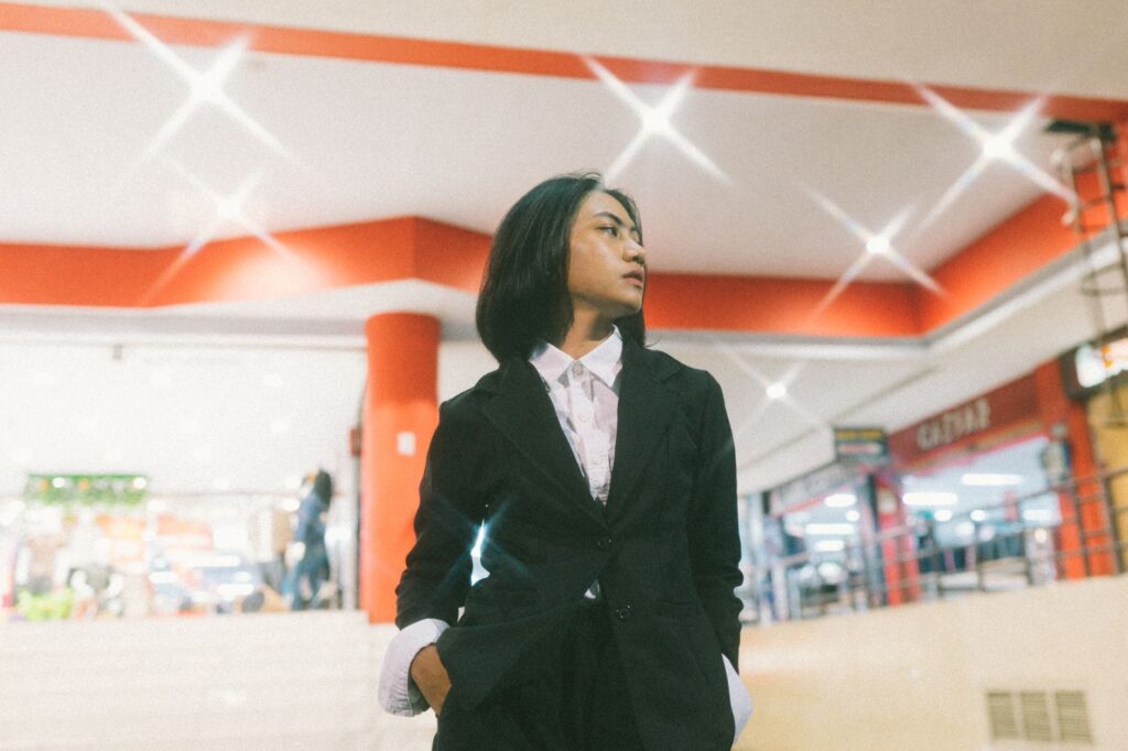 Young woman in a suit confidently posing indoors with bokeh lights.