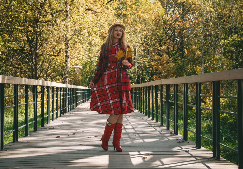 Woman in red plaid dress walking on bridge during fall season, surrounded by colorful autumn foliage.