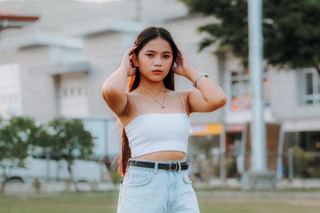 Stylish young woman in white tank and jeans posing confidently outdoors.