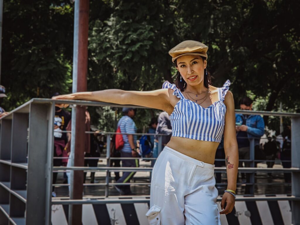 Confident woman poses in street style attire with a striped crop top and cap outdoors.